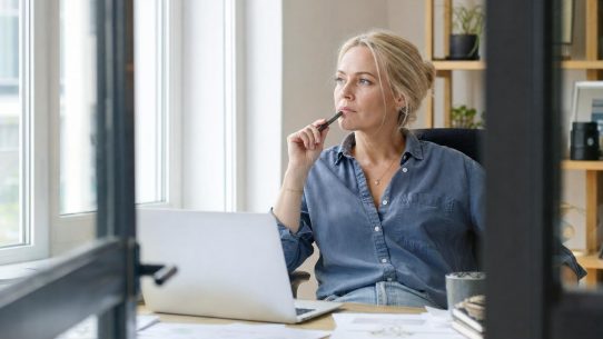 Femme réfléchissant devant ordinateur portable au bureau