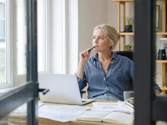 Femme réfléchissant devant ordinateur portable au bureau